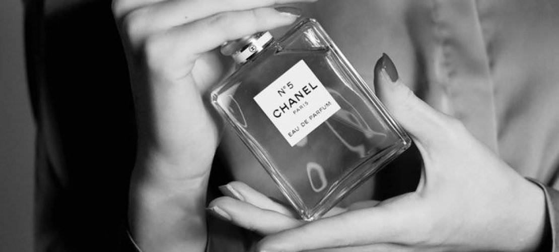 Black and white image of a woman holding a Chanel perfume bottle in a satin blouse.