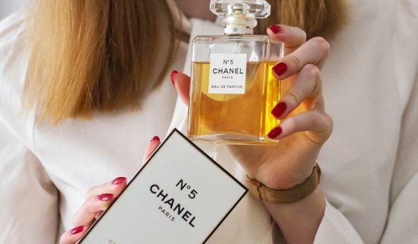 Woman displaying Chanel No.5 perfume against a neutral background with elegant attire.